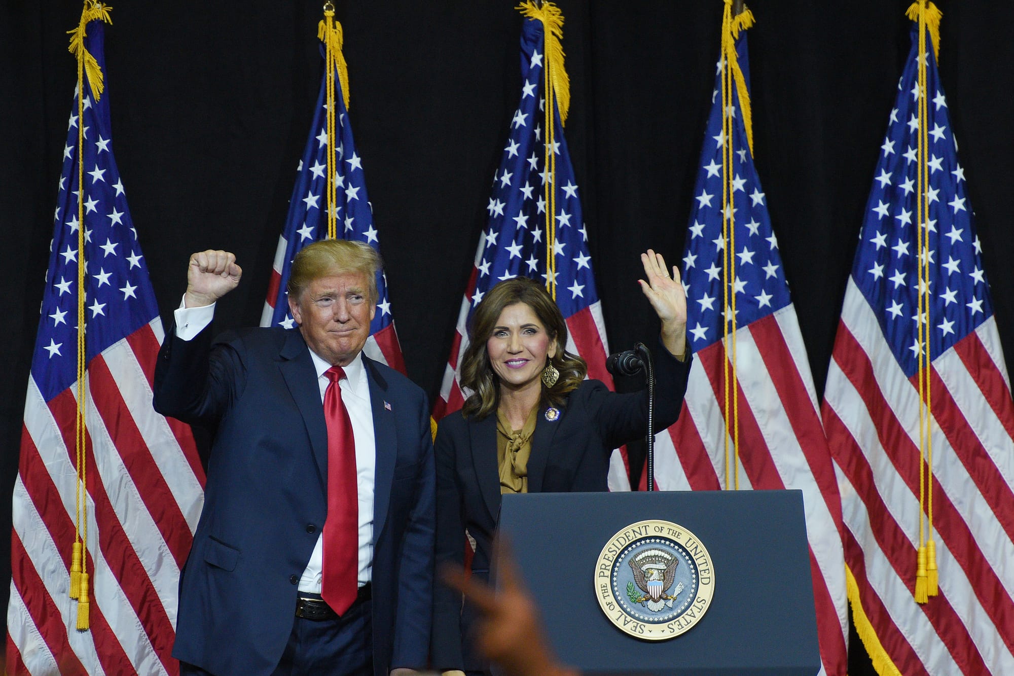Donald Trump stands with South Dakota Kristi Noem in front of a row of flags 