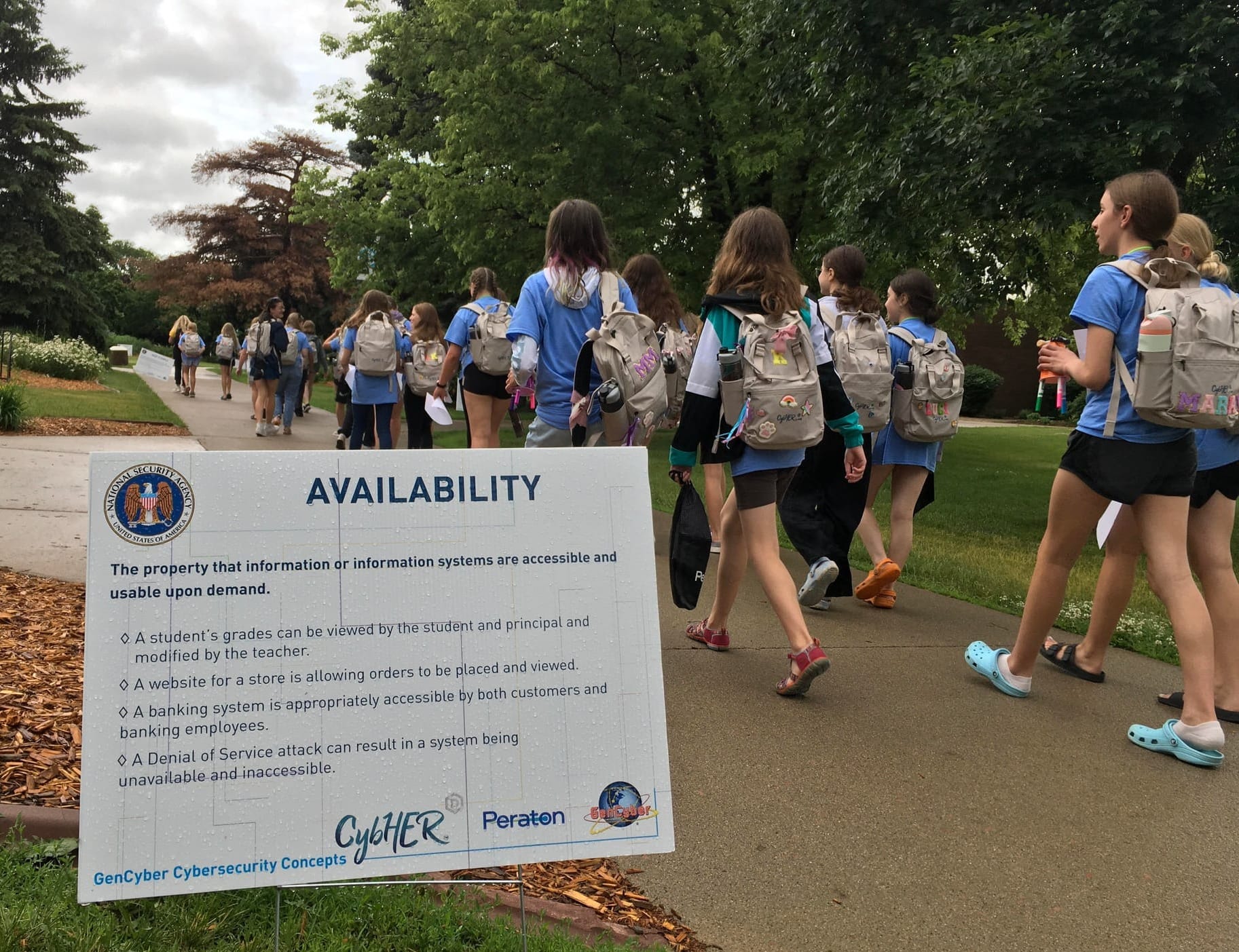 Girls walk by a CybHER camp poster at Dakota State University