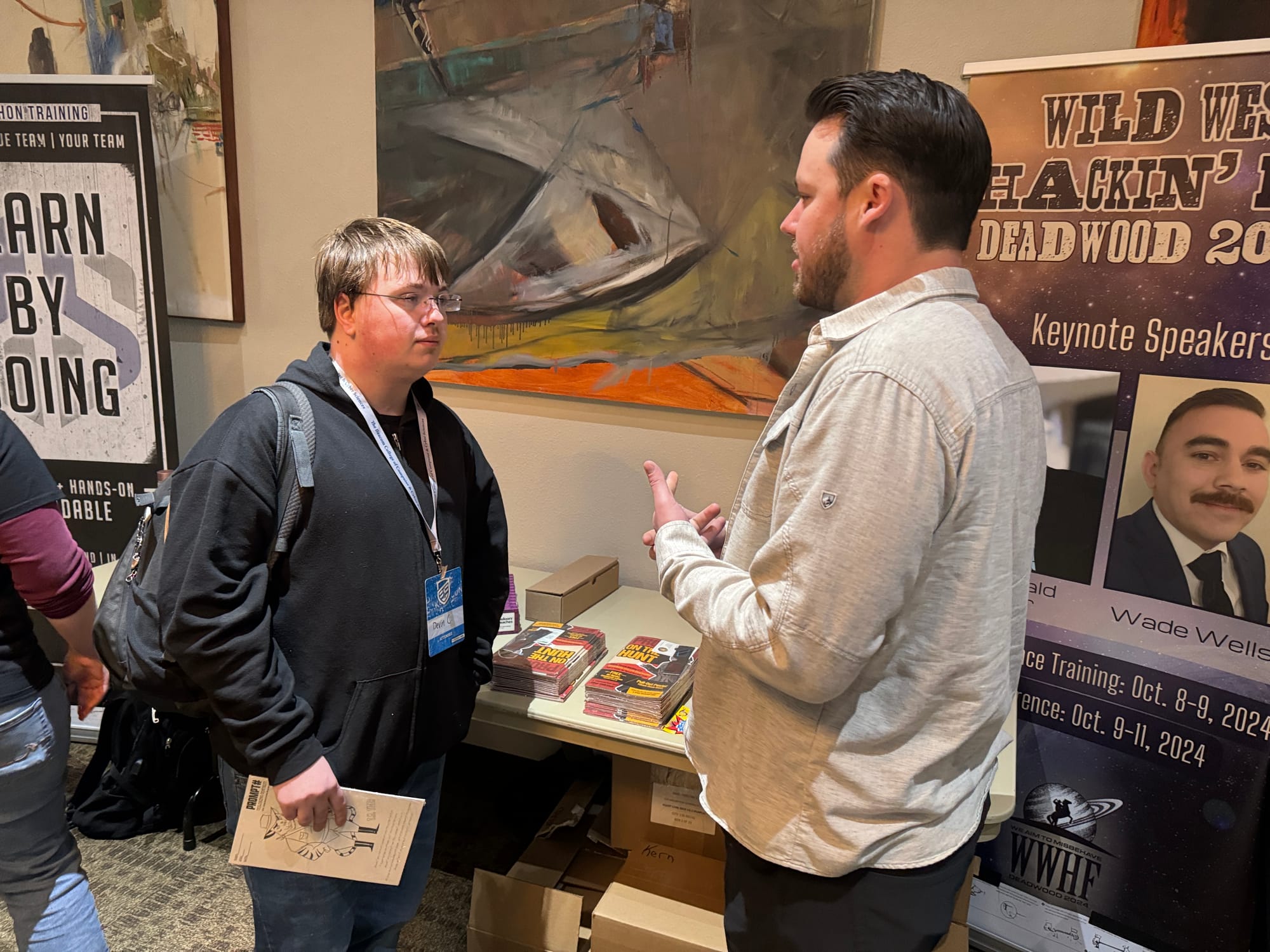 Two men talk in front of paintings at DakotaCon at Dakota State University.