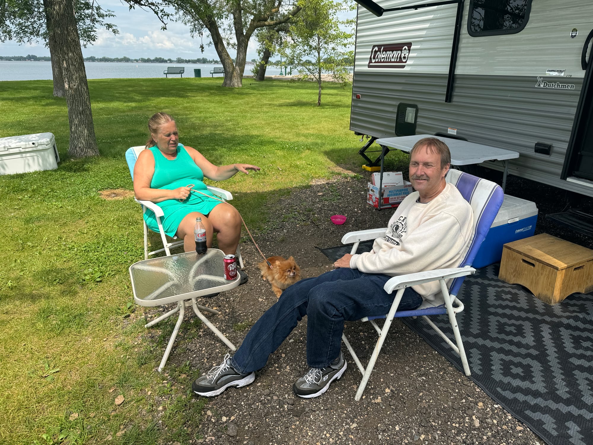 A man and a woman sit in chairs outside an RV on a lake in South Dakota