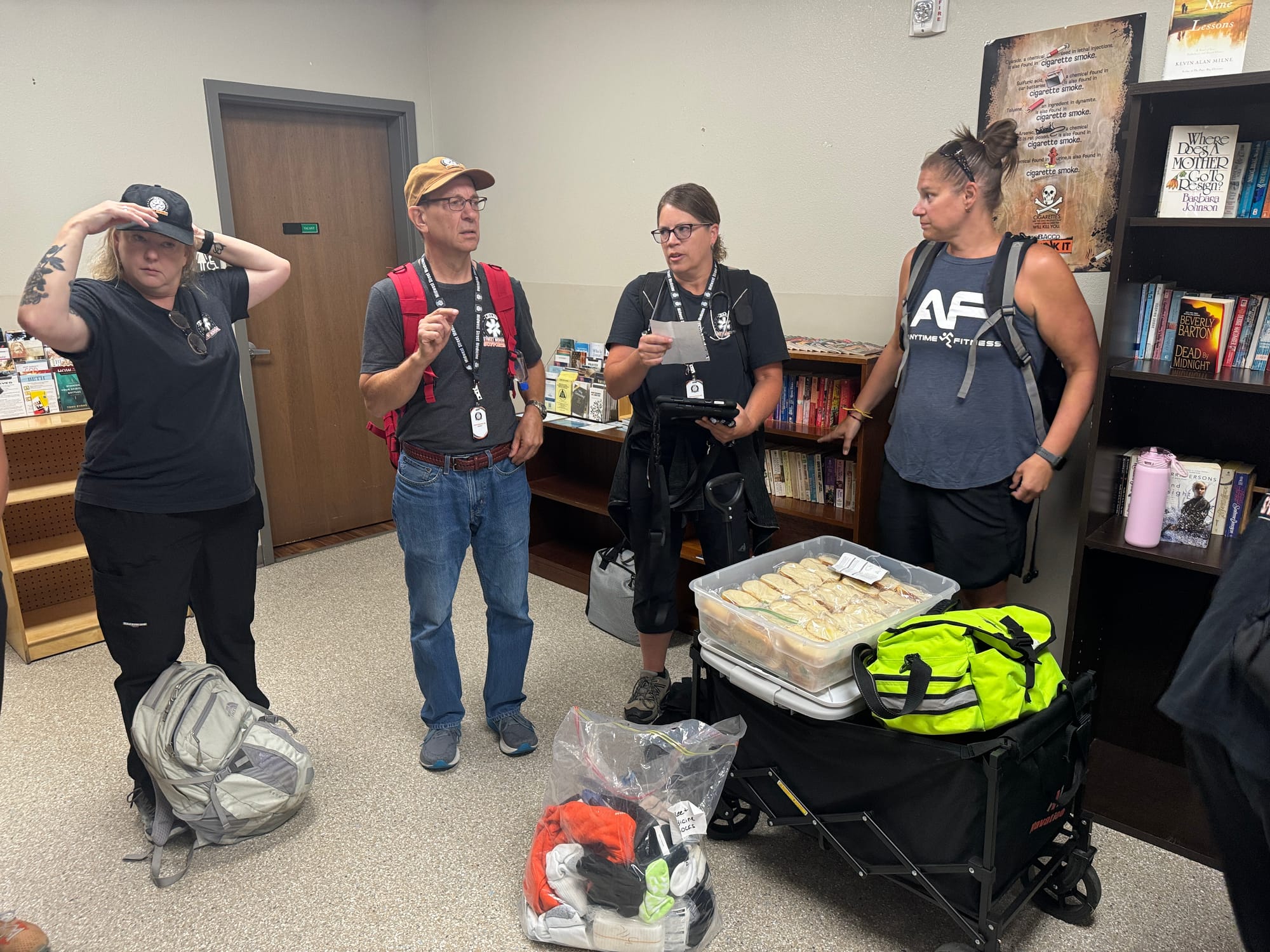 A group of four people from the Midwest Street Medicine volunteer group stand and talk in a small room filled with books and other reading material.