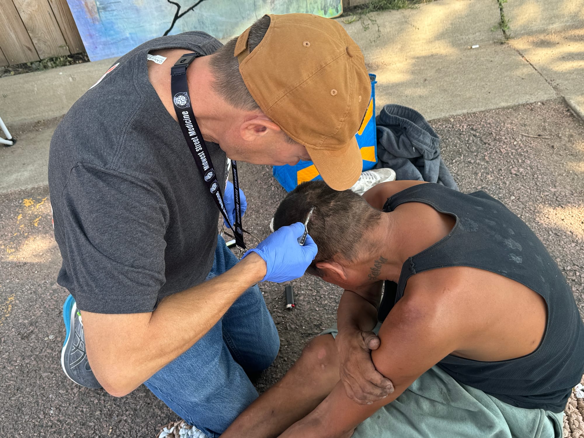 A doctor removes staples from the head of a homeless man on the pavement in Sioux Falls, South Dakota.