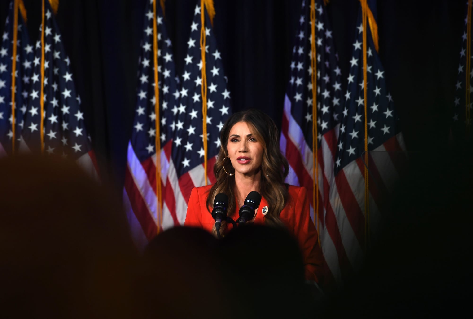 South Dakota Gov. Kristi Noem stands in front of a row of flags while greeting supporter.