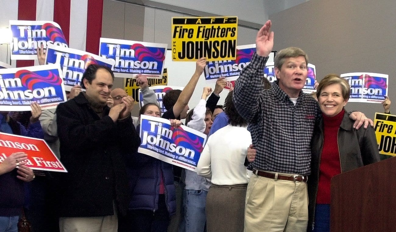 South Dakota Sen. Tim Johnson stands with his wife while people hold his campaign signs in the background