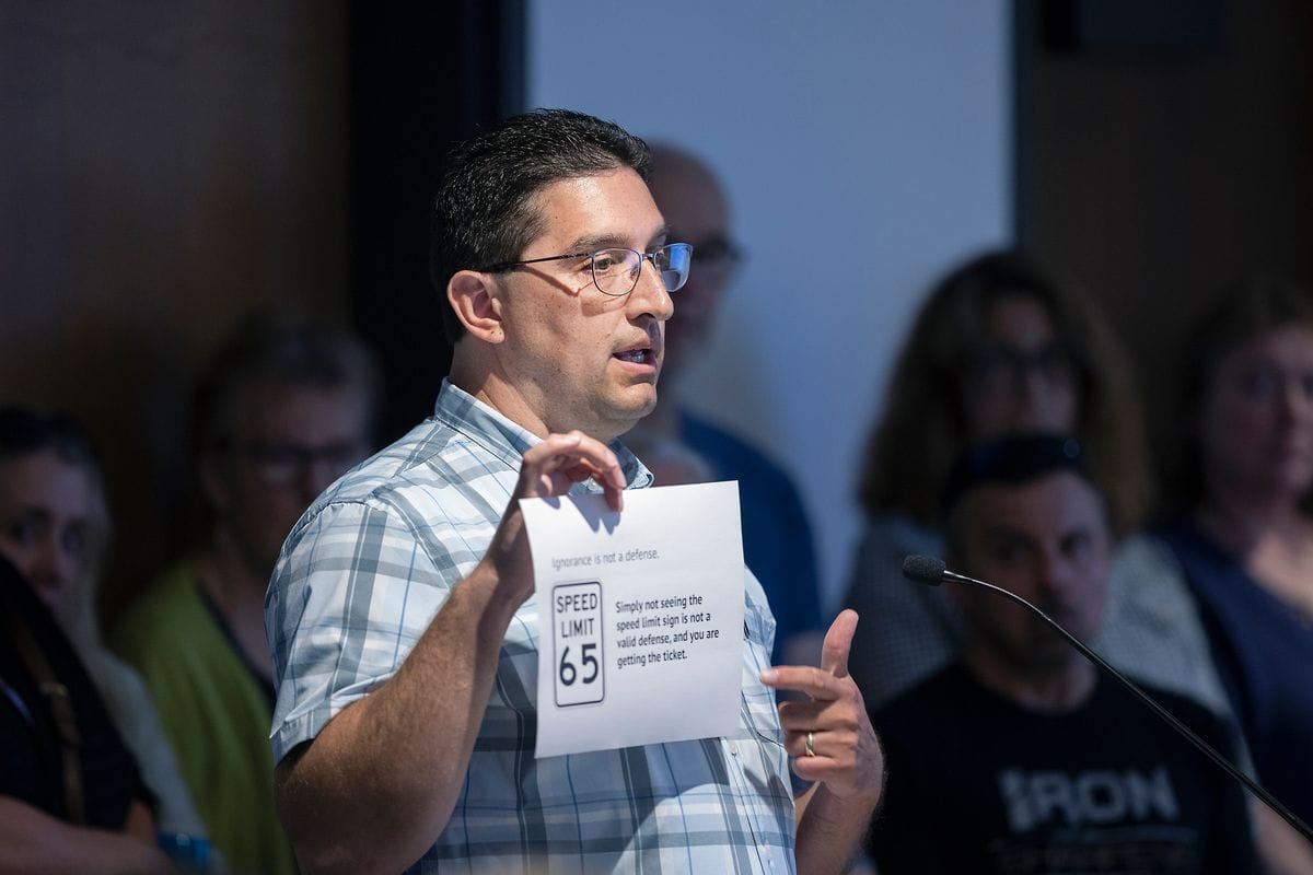 A man stands at a podium speaking while holding a piece of paper