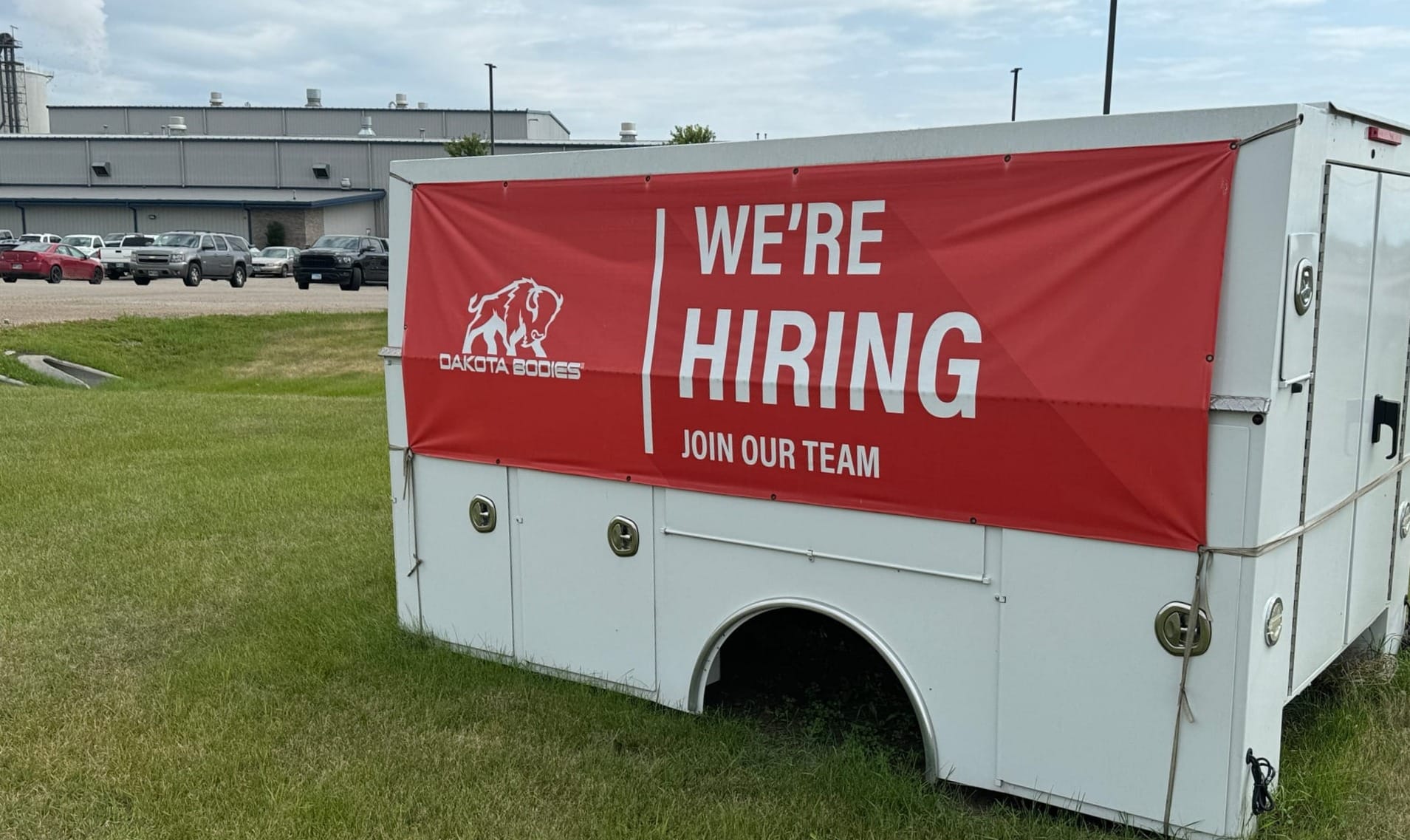 A sign outside the Dakota Bodies Manufacturing plant says "we're hiring, join our team."