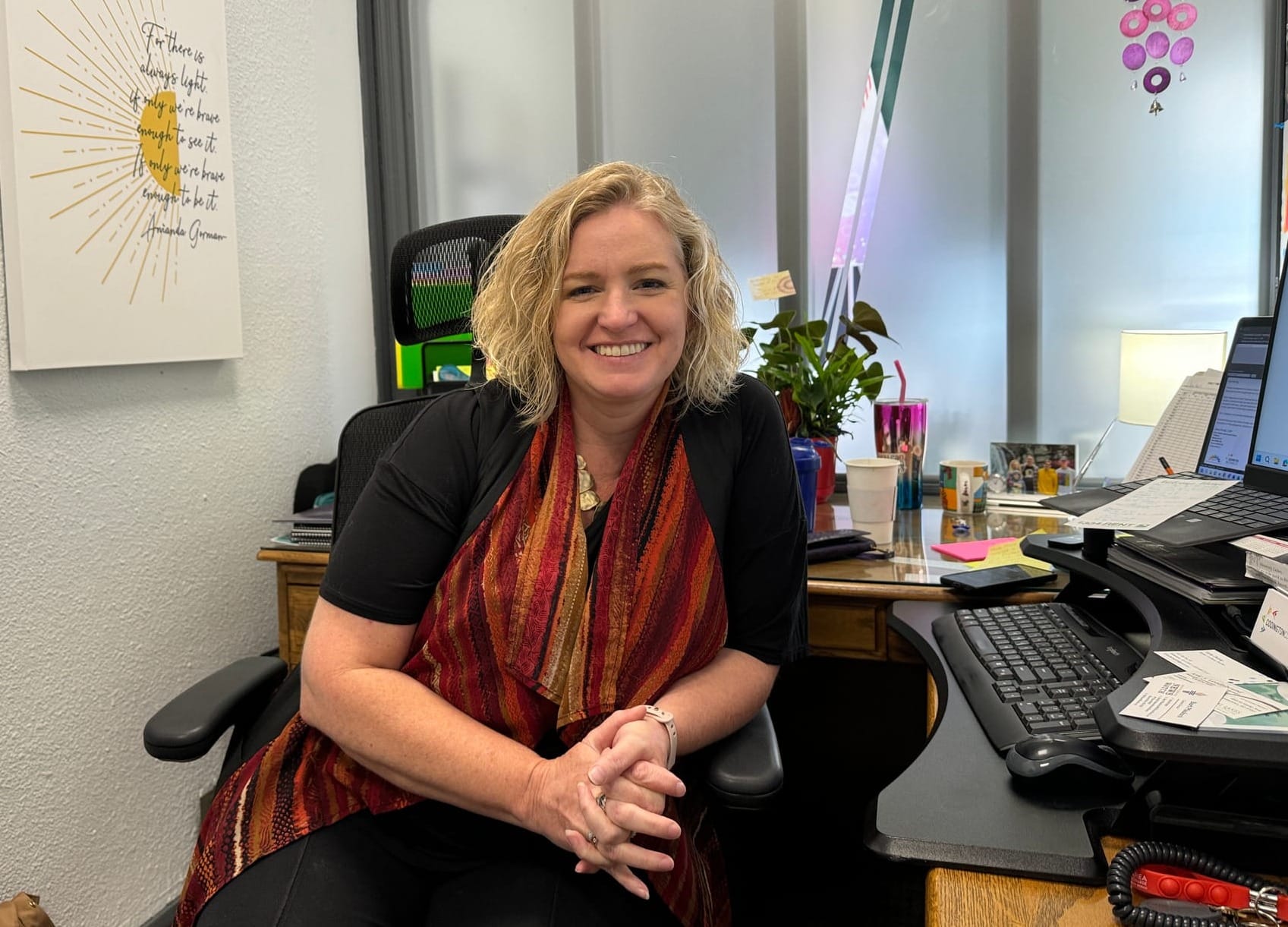 Sara Foust sits at her desk and faces toward the camera, smiling. 