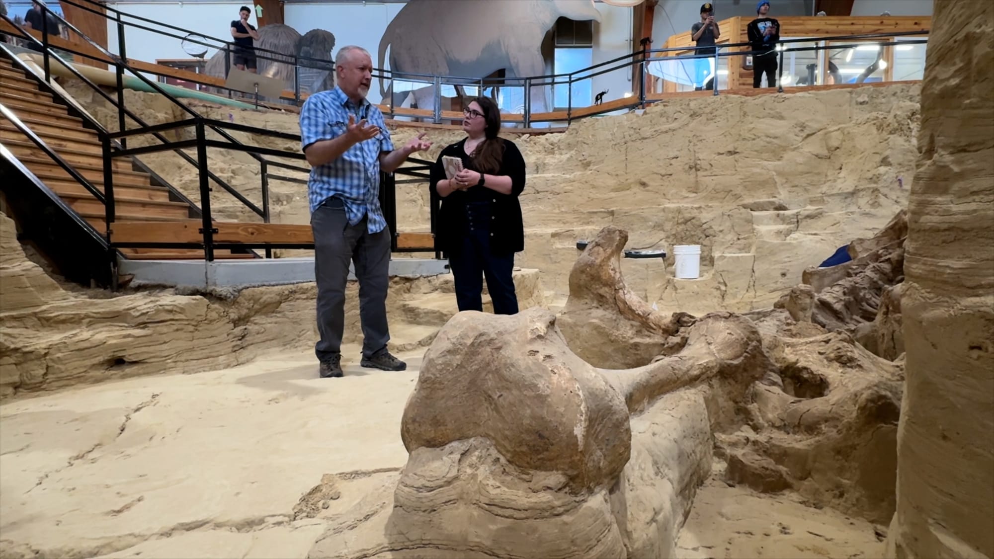 Mammoth Site lead researcher Chris Jass and SDPB's Jackie Hendry stand next to one of the mammoth fossils in the active dig site in Hot Springs, S.D., on July 17, 2024. 