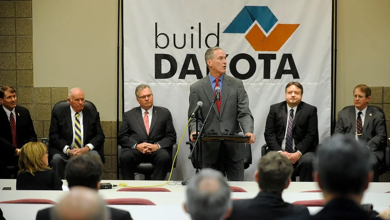 Gov. Dennis Daugaard stands at a podium in front of a group of college students and other dignitaries.