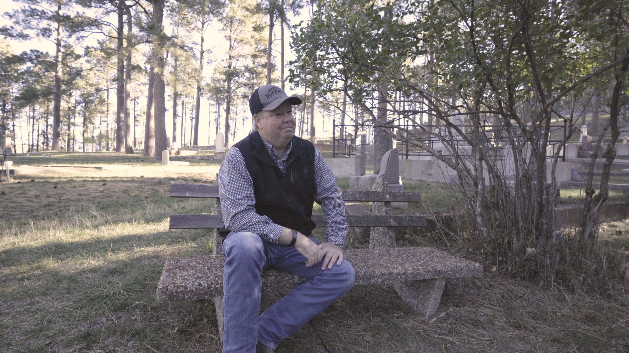 A man sits on a bench in a forested area in Deadwood, South Dakota.