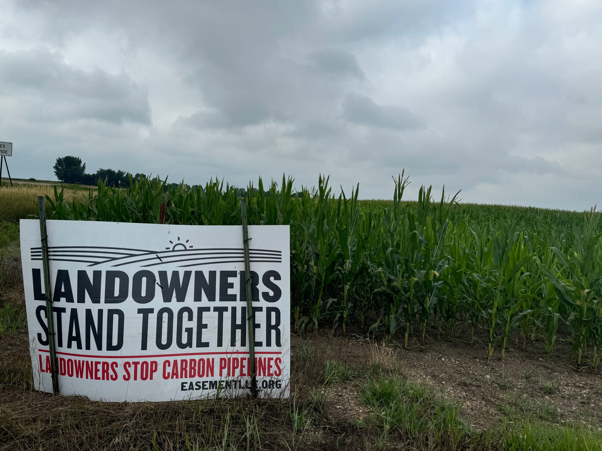 A sign urging landowners to stand together against eminent domain and carbon pipelines is displayed next to a corn field