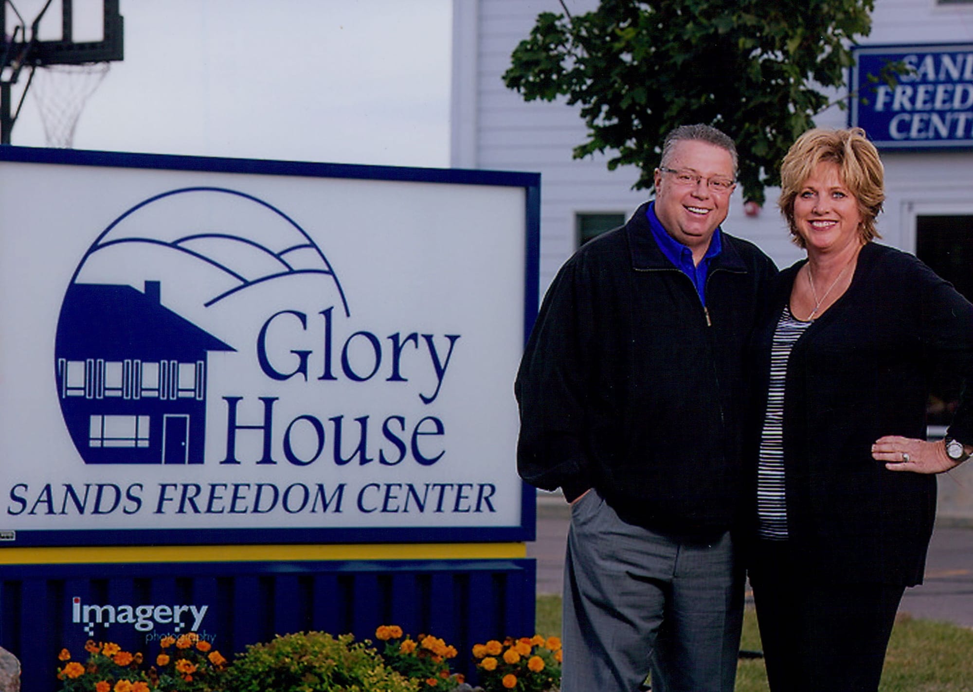 Pam and Greg Sands standout next to a Glory House Sands Freedom Center sign