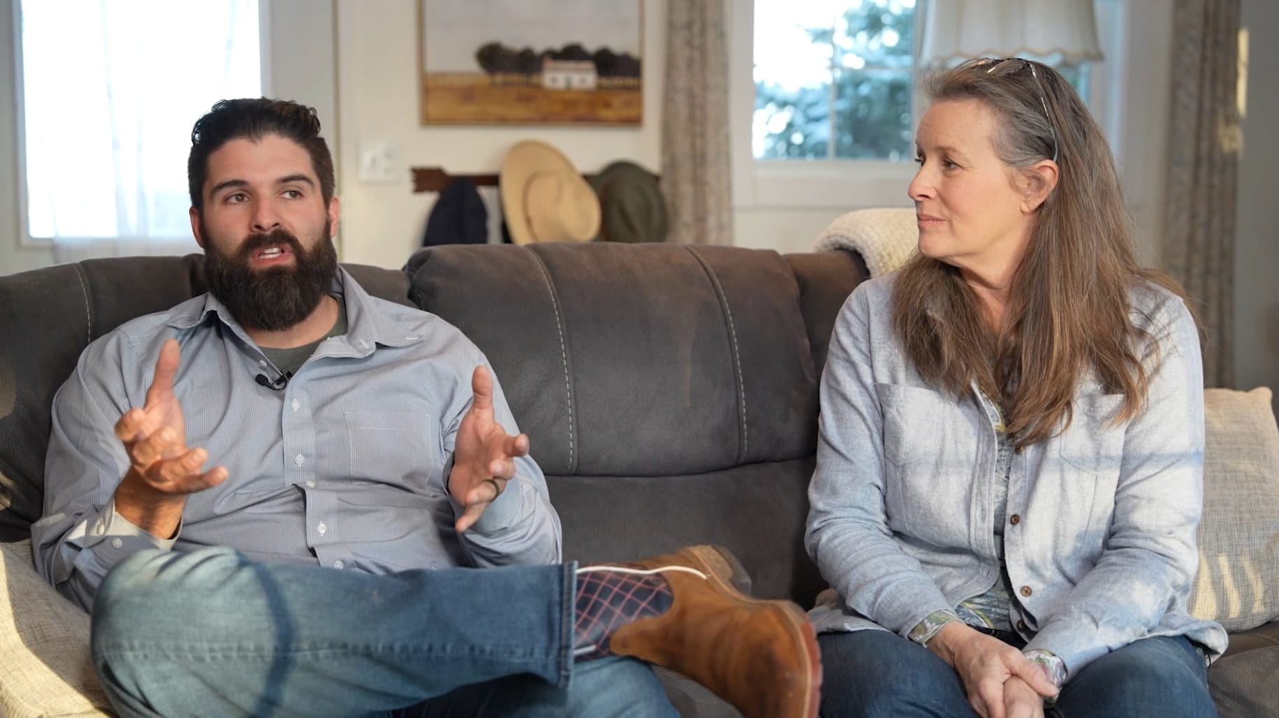 Nathan Derksen (left) and Kristin Bennett (right) sit on a couch and Nathan gestures toward the camera