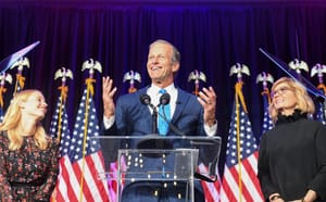 South Dakota Sen. John Thuen stands and smiles in front of a row of American flags after being re-elected to the Senate