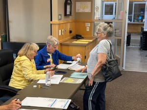 A woman stands at a table as her voter registration information is checked by two women during an election in Sioux Falls