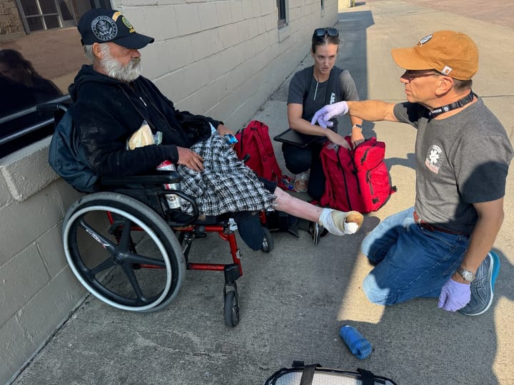 A doctor and a nurse help a homeless man in a wheelchair with his foot in an alley in Sioux Falls, South Dakota.