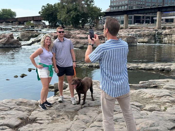 A man and a woman pose for a photo taken by another person at Falls Park in Sioux Falls, South Dakota.