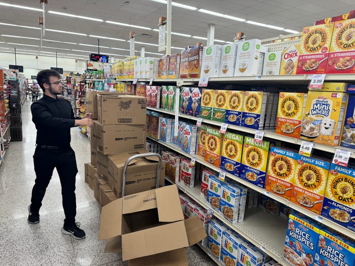 A man stocks groceries in the cereal aisle of a grocery store.