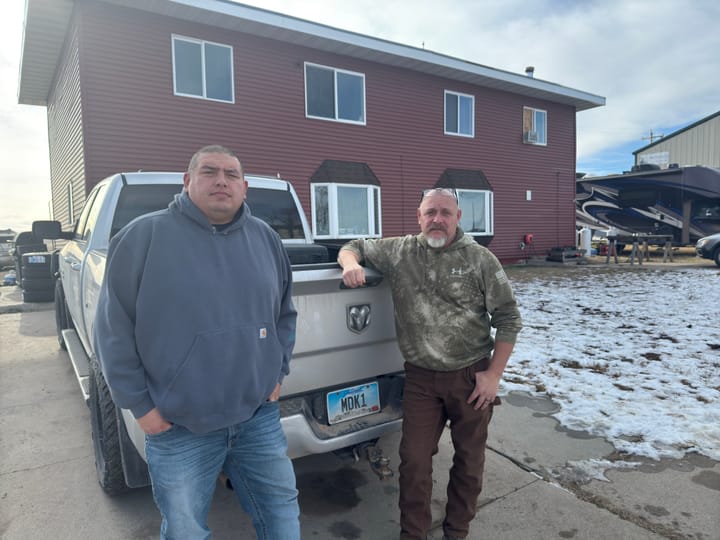 Two men stand behind a truck outside a home in Igloo, South Dakota.