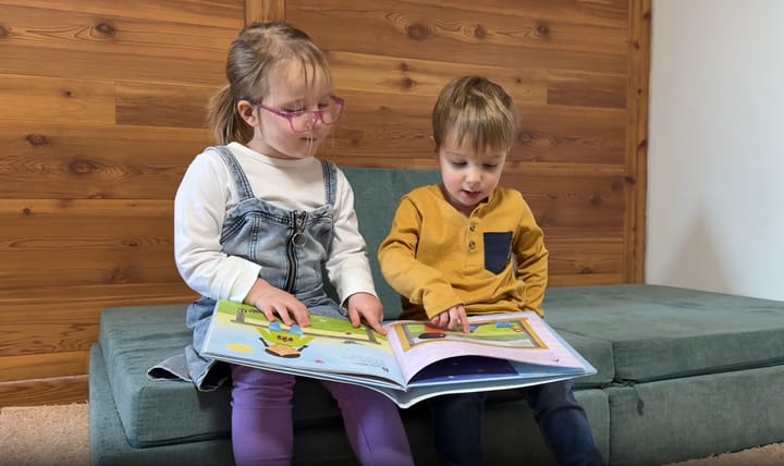 Two kids sit on a chair and read a book together