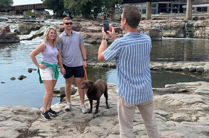 A man and a woman pose for a photo taken by another person at Falls Park in Sioux Falls, South Dakota.